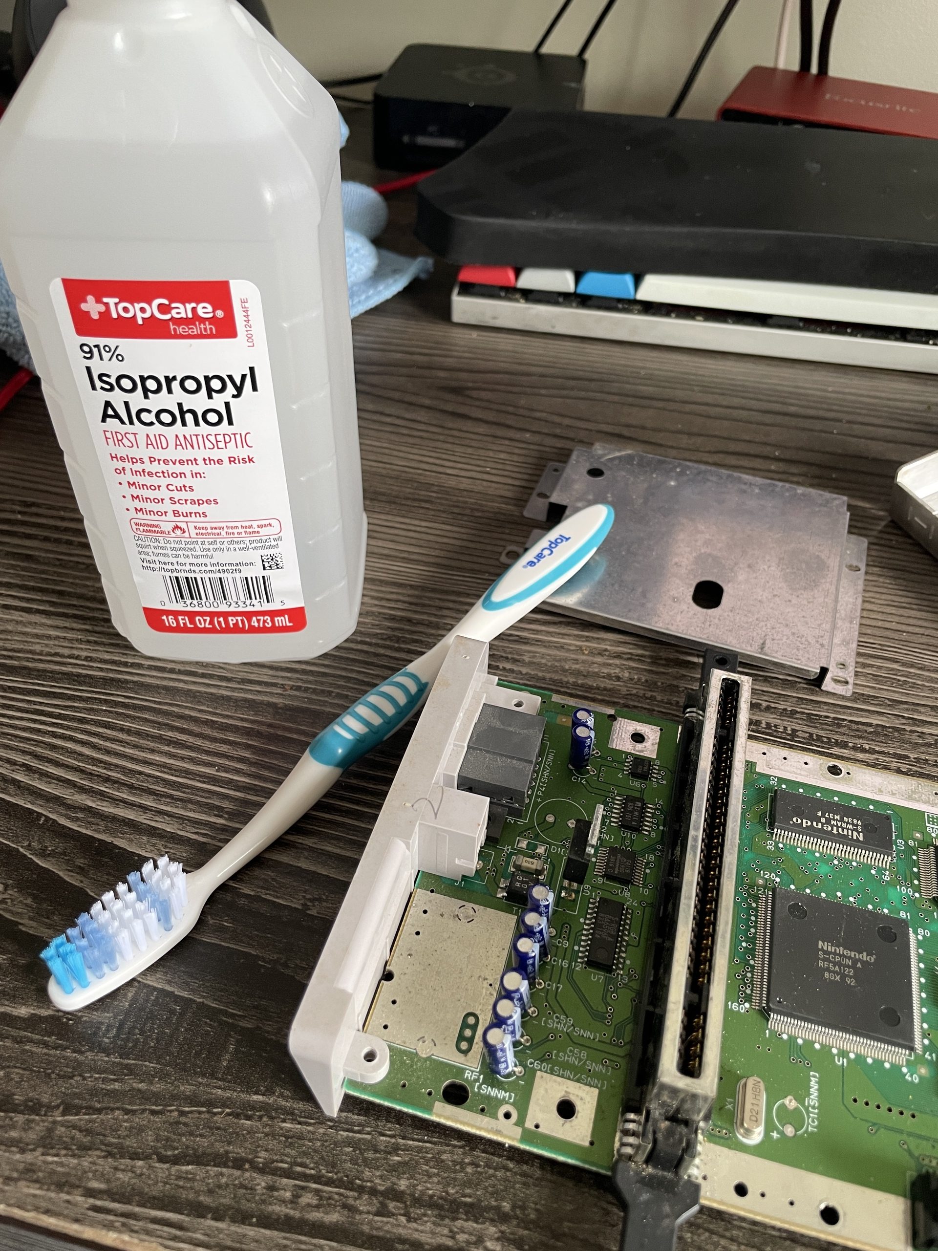 The half of the SNES Jr. motherboard with the power and AV I/O, along with a toothbrush and isopropyl alcohol.